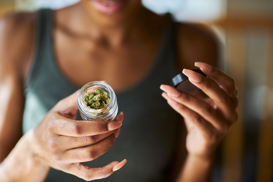 Person holding a small glass jar of cannabis